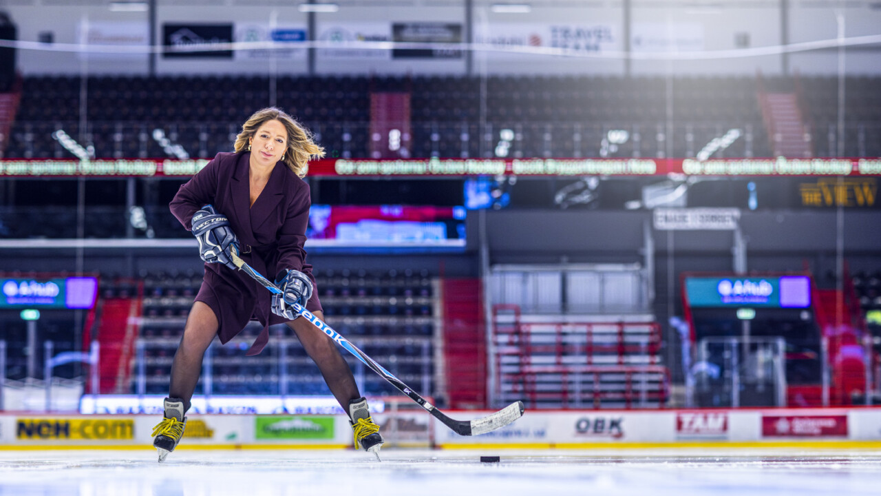 Jennifer Mayer klädd i vinröd klänning med hockeyklubba, puck och skridskor inne i rinken på Behrn Arena i Örebro.