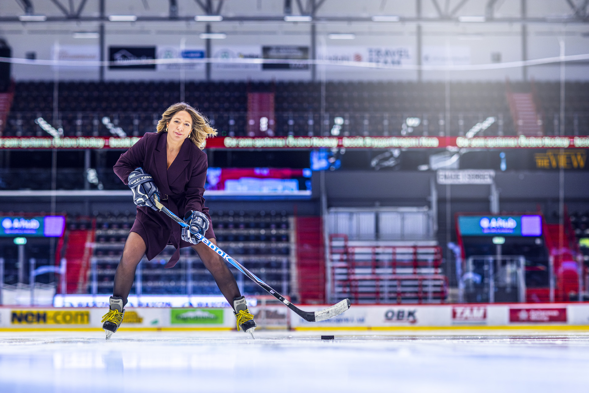 Jennifer Mayer klädd i vinröd klänning med hockeyklubba, puck och skridskor inne i rinken på Behrn Arena i Örebro.